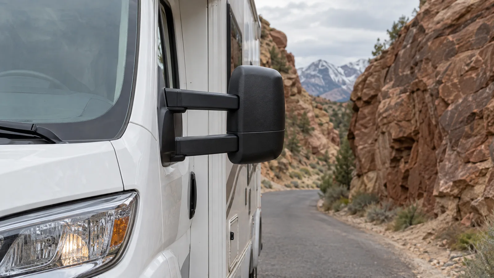 A close view of a motorhome's extended side mirror against a narrow rock passage